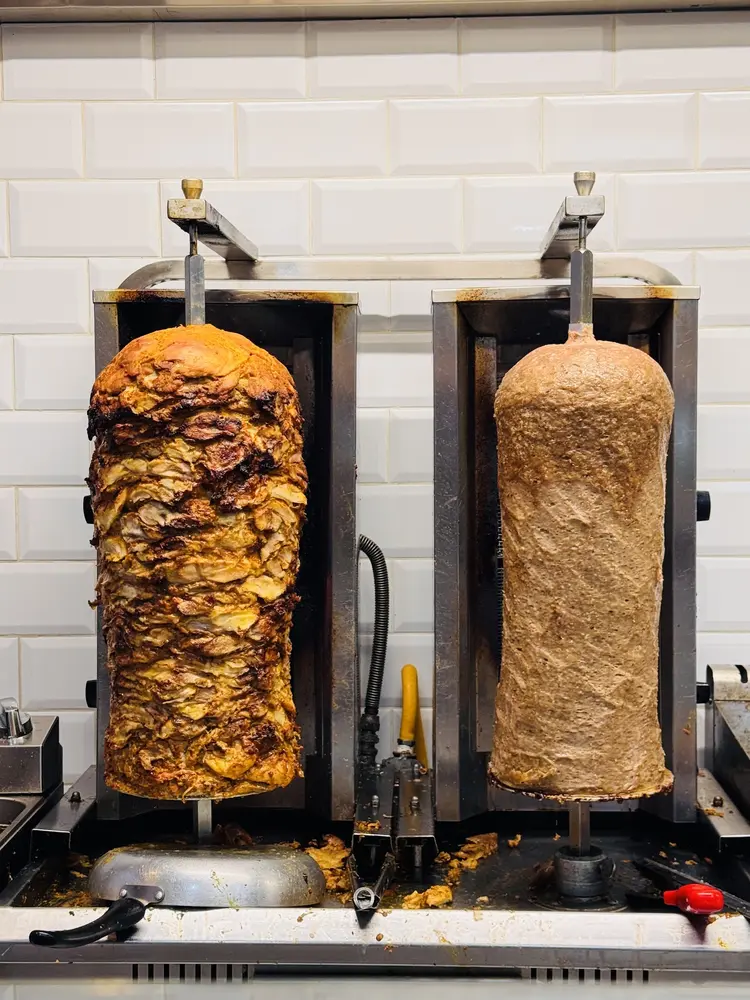 Two shawarma spits, chicken and lamb, turning in front of the grill