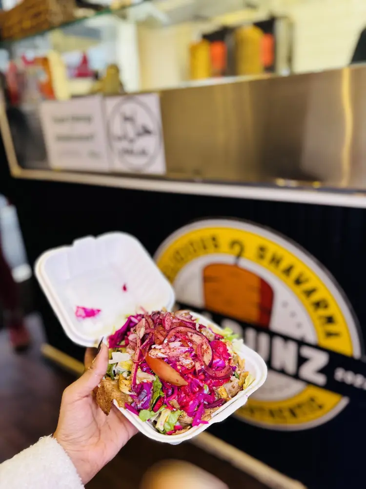 Hand holding an open shawarma box in front of the yellow Holbunz logo